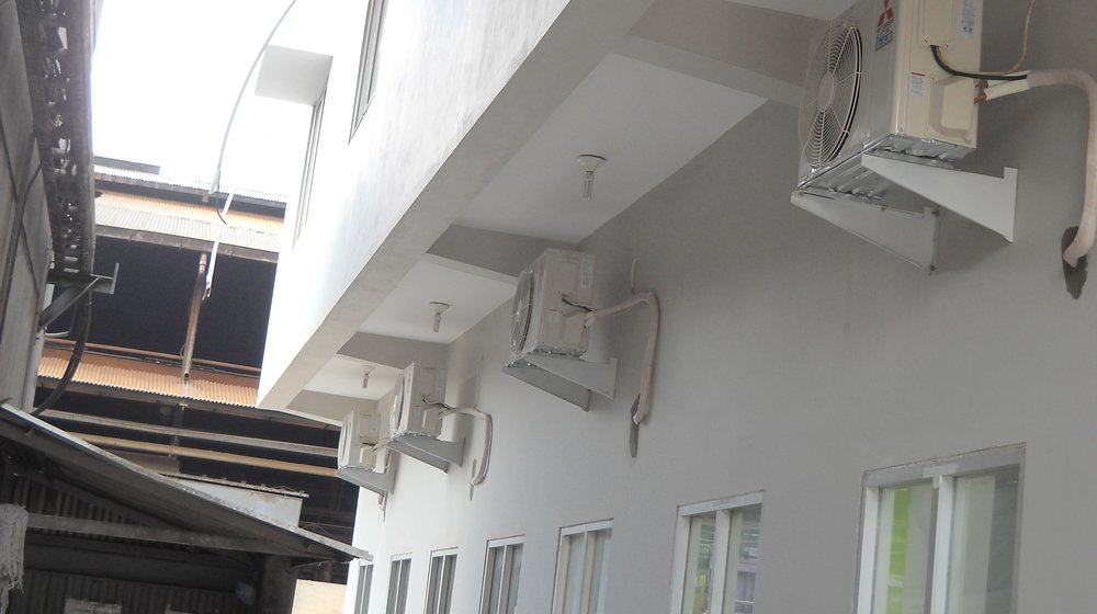 Unit outdoor AC yang terpasang di bawah kanopi pada dinding luar bangunan